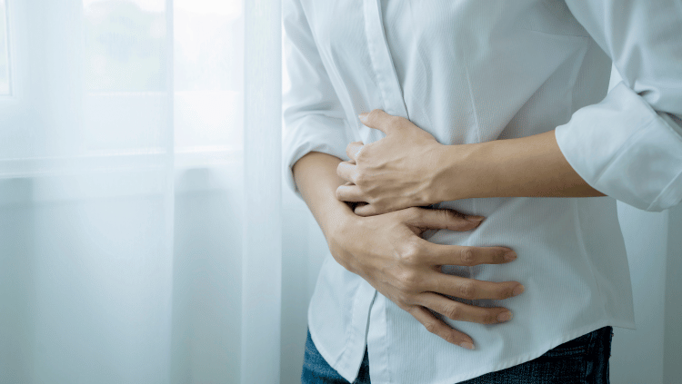Woman in a white button down holding their stomach in pain