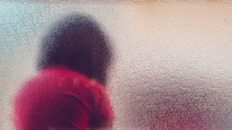 person in red shirt leaning their back against a glass wall