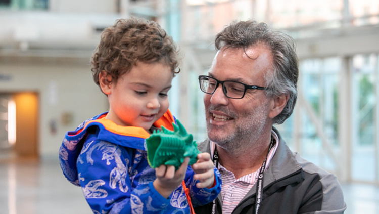 A man holds a young boy, who is playing with a neuroscience toy at Neuroscience 2022 in San Diego.