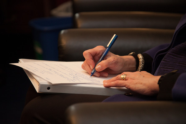 Image of a person taking notes at a legislative meeting.