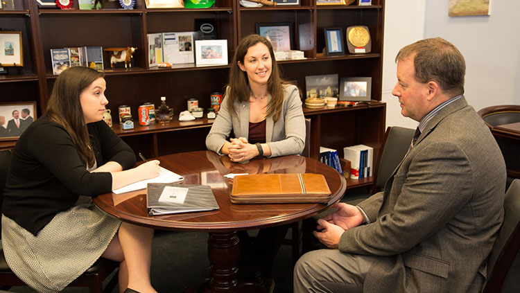 Image of three people sitting around a round, wood table smiling and having a conversation.