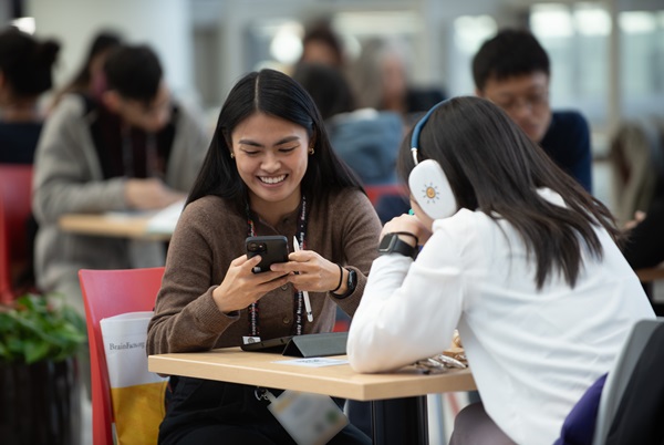 Two attendees seated at a table looking at a phone and smiling