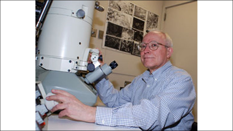 Image of Donald Morest sitting at a microscope wearing a blue button down shirt.
