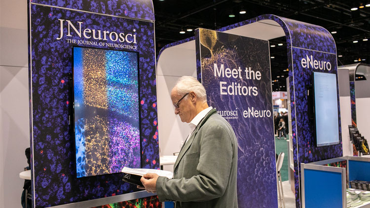 Attendee looking at a copy of JNeurosci at the SfN booth in the exhibit hall of Neuroscience 2019