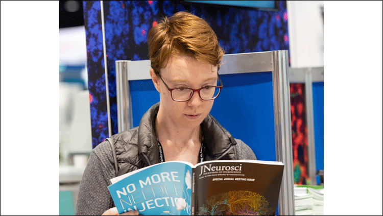 Person reading a printed copy of JNeurosci at the annual meeting